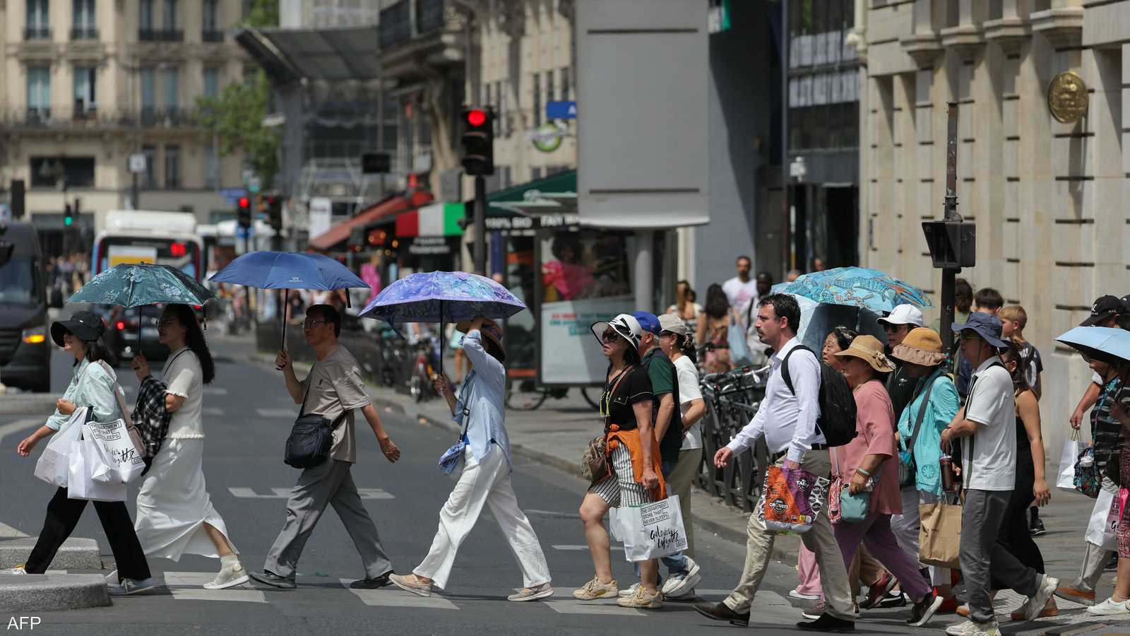 يحتمي السياح من أشعة الشمس أثناء عبورهم أحد شوارع باريس